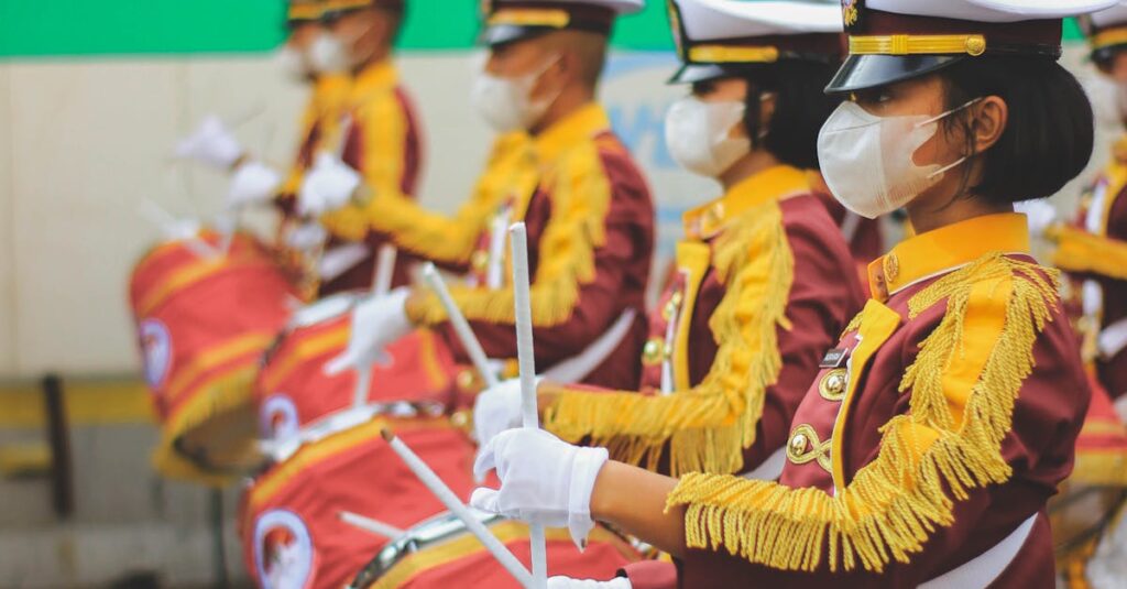 Marching band members perform in Jakarta street parade, wearing maroon and yellow uniforms with masks.